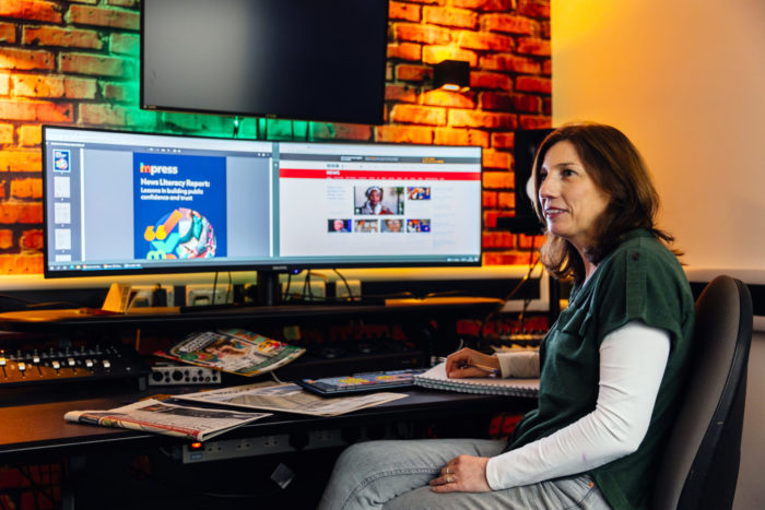 Photograph of Julie Firmstone in a media studio with display screens and newspapers