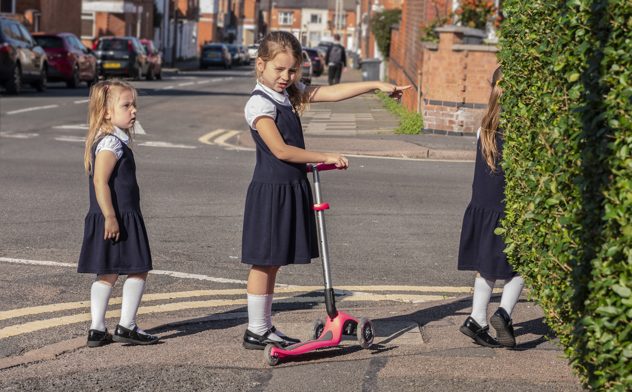 Young school children in street with a scooter