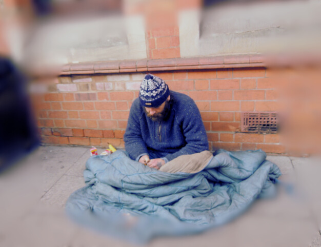 Photo of a homeless man sitting under a sleeping bag in the street
